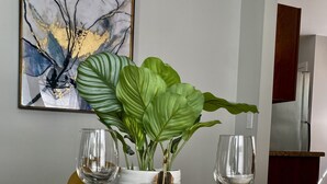 A dining table set with white plates, bowls, and wine glasses, surrounded by a large green plant and decorative jars. - Beautiful Modern House 5 minutes To Downtown Raleigh (Raleigh)