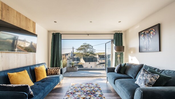 Un salon moderne avec deux canapés, un tapis à motifs géométriques et une vue sur la ville grâce à de grandes fenêtres.