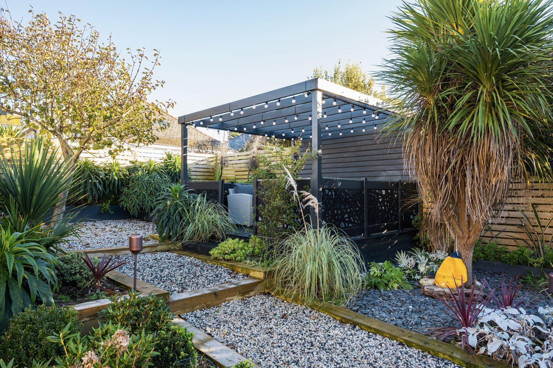 Un jardin agrémenté d’une pergola, de différentes plantes et d’un sentier.