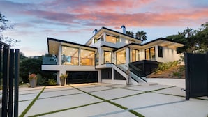 Une maison moderne à deux étages, dotée de grandes fenêtres en verre, d’un espace extérieur couvert et d’un escalier menant à l’étage supérieur.