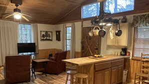 Un accogliente interno di una baita con pavimento in legno, zona pranzo con tavolo e sedie, cucina con isola in legno e televisione nella zona soggiorno.