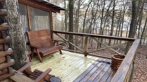Un patio in legno con panchina e sedie, immerso tra gli alberi.