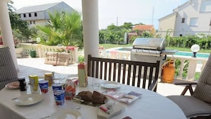 An outdoor dining area with a table set for four, surrounded by chairs. A grill and a pool are visible in the background. - Villa Irmica - Impressive pool, spacious apartment (86 m²) - first floor (Donja Jagodnja)
