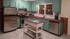Een keuken met smaragdgroene kastjes, een roestvrijstalen koelkast, een kookplaat, een spoelbak en een koffiezetapparaat.