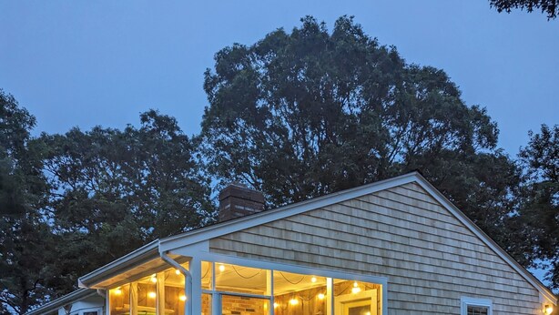 Een houten huis met een glazen veranda, een terras en zitplaatsen buiten.