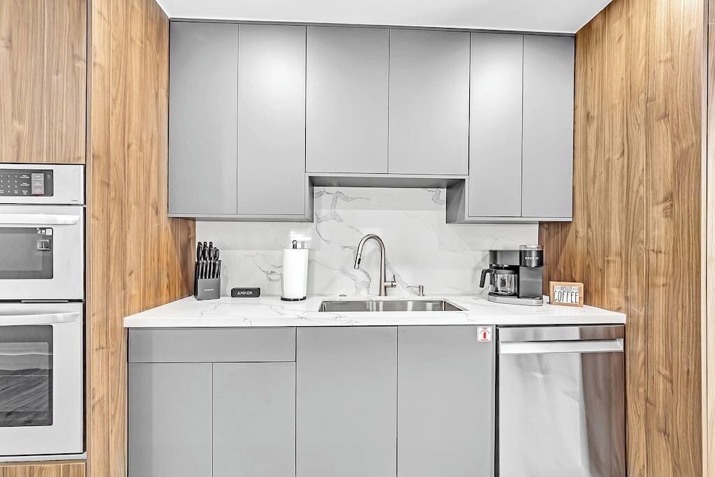 Una cocina moderna con armarios grises, encimera blanca, pileta de acero inoxidable y lavavajillas.