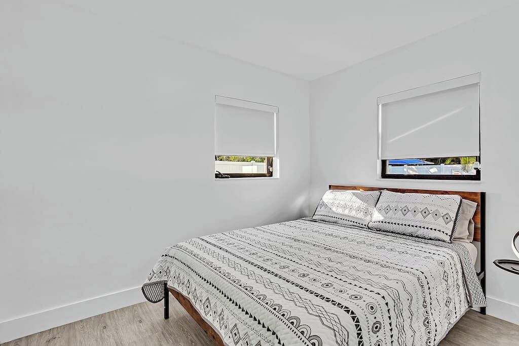 A bedroom with a bed, a headboard, a window, and a mirror.