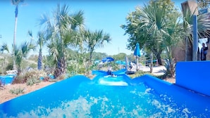 Um tobogã com piscina azul cristalina na base, cercado por palmeiras e céu ensolarado.