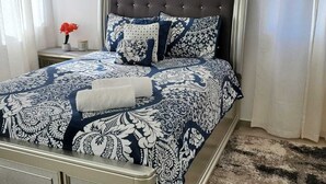 Un dormitorio con cama, una mesita de noche, una cita enmarcada en la pared y una ventana con cortinas.