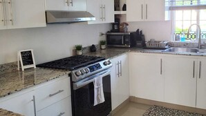 Una cocina moderna con armarios blancos, estufa a gas, horno empotrado y campana extractora de acero inoxidable.