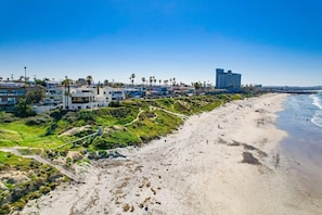 Um hotel à beira-mar com vários edifícios, uma praia arenosa e um cais ao fundo.