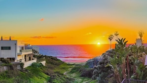 A coastal sunset view with modern buildings and a path leading to the beach.