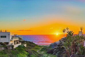 Une vue sur le coucher de soleil en bord de mer, avec des bâtiments modernes et un sentier menant à la plage.