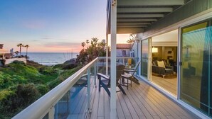 A balcony with a view of the ocean, outdoor seating, and a sliding glass door leading to a room.