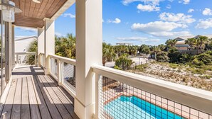 Um deck de madeira com piscina e vista para uma área residencial com casas e palmeiras.