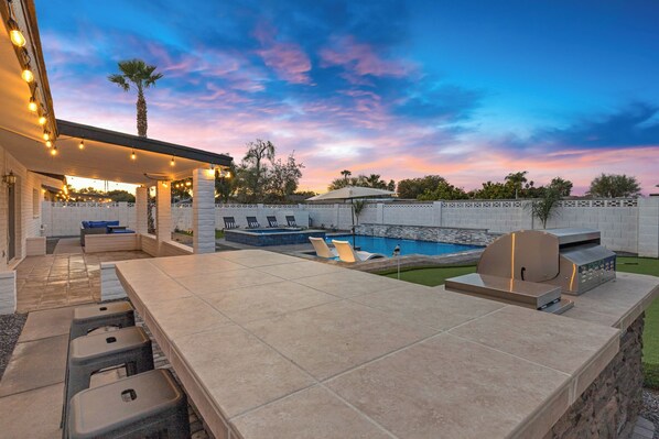 A backyard with a pool, outdoor seating, and a barbecue area.