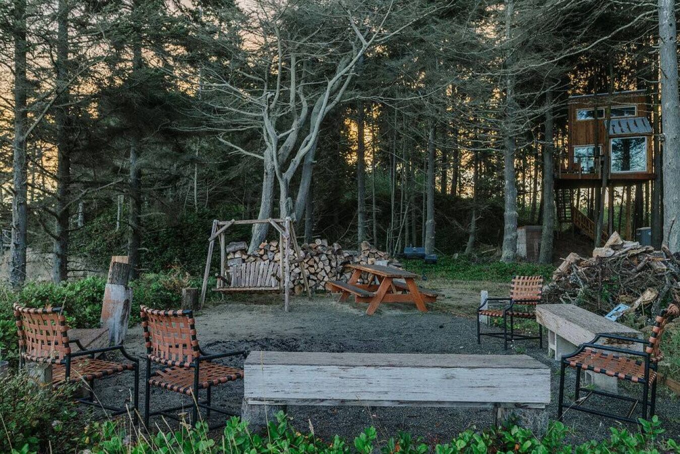 A rustic outdoor seating area with a swing, a picnic table, and a wooden bench.