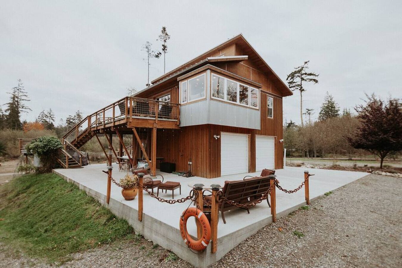 Une maison en bois à deux étages, dotée d’un balcon, d’un garage et d’une terrasse en béton.
