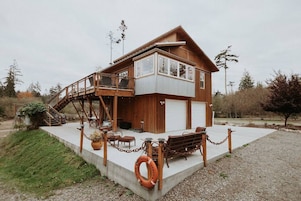 Una casa de madera de dos pisos con balcón, garaje y un patio de concreto.