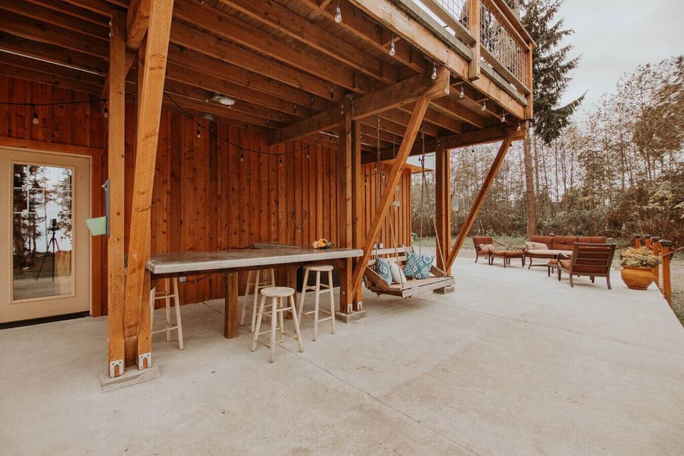 A wooden outdoor seating area with a table and stools, a swing, and a sofa.