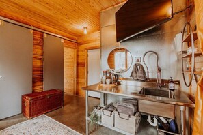 A wooden cabin interior with a wooden floor, a wooden bench, a sink with a mirror, and a towel rack.