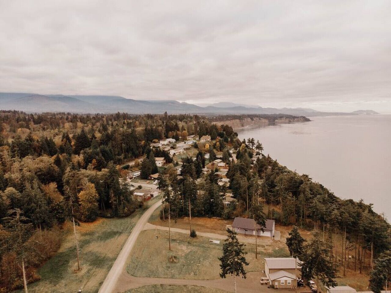 Vue aérienne d’une zone résidentielle côtière, avec des maisons, une route et une étendue d’eau.