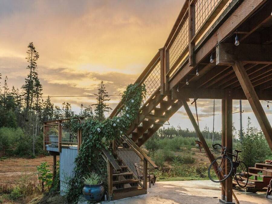A rustic wooden staircase leading to a covered area with a bicycle and a wooden bench.
