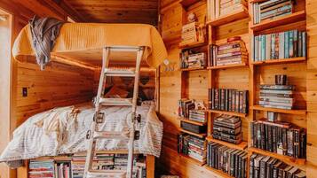 A cozy cabin with a bunk bed, a ladder, and a bookshelf filled with books.