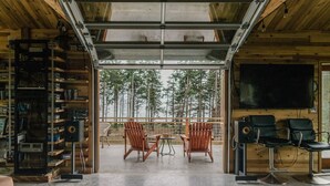 En mysig stuga med en stor fönsterruta som vetter ut mot en skog, träväggar, en bokhylla och en tv.