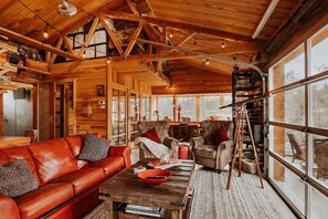 A cozy log cabin interior with a red leather sofa, a wooden coffee table, and a ladder leaning against the wall. - Eagle's Landing (Port Angeles)