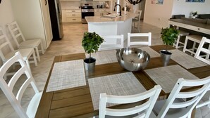 A modern kitchen with white cabinets, a central island, and a dining area with a wooden table and white chairs. - The Villages 3 bed/3 Kings, Private, Coastal decor, 1 min to Rec cntr & Pickleba (The Villages)