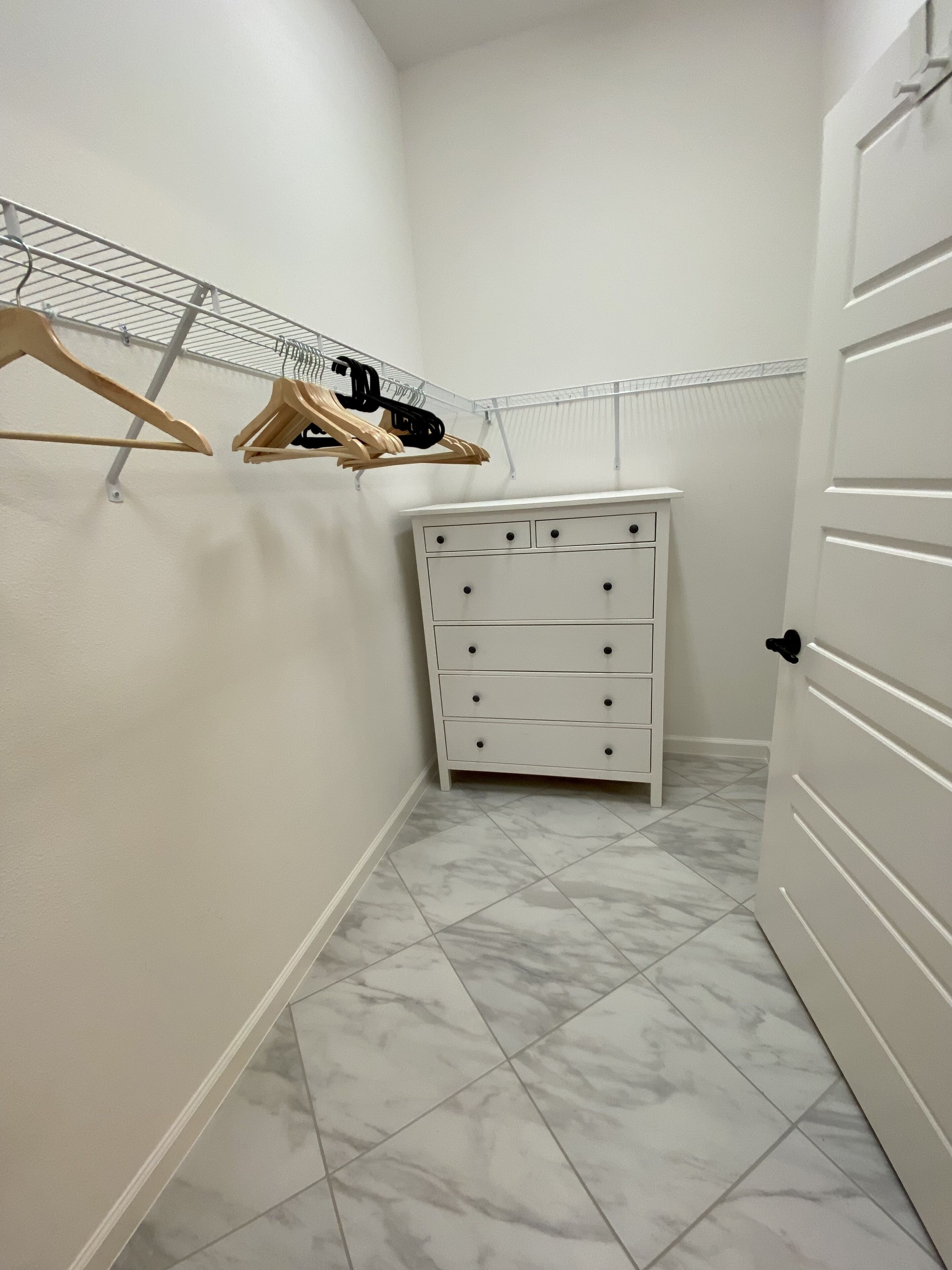 A narrow hallway with a white dresser, a metal drying rack, and a door.
