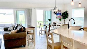 A modern kitchen with a central island, dining area with chairs, and a sofa with cushions. - The Villages 3 bed/3 Kings, Private, Coastal decor, 1 min to Rec cntr & Pickleba (The Villages)
