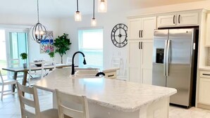 A modern kitchen with a central island, white cabinetry, stainless steel appliances, pendant lighting, and a clock on the wall. - The Villages 3 bed/3 Kings, Private, Coastal decor, 1 min to Rec cntr & Pickleba (The Villages)