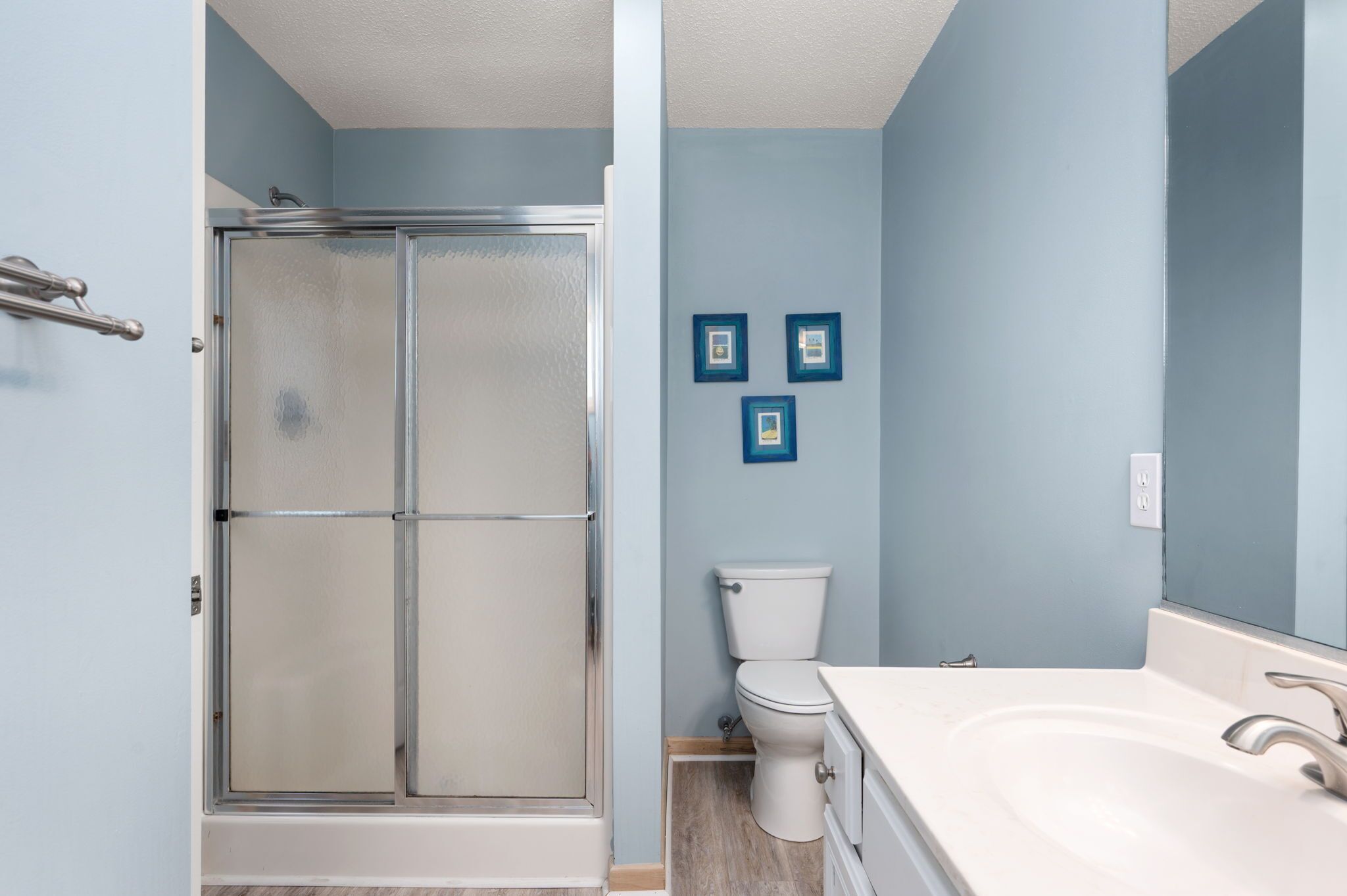 A bathroom with a glass shower enclosure, a toilet, and a sink with a mirror.