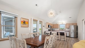A modern kitchen with a wooden dining table, white chairs, and a stainless steel refrigerator. - Oceanside, Lovely, New home! Sat-Sat (Corolla)