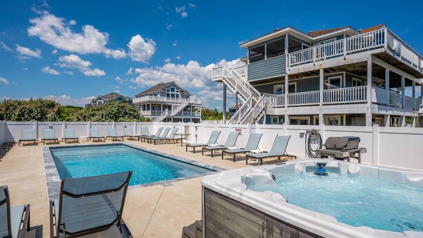A pool area with lounge chairs, a hot tub, and a multi-level building with balconies. - Oceanside, Lovely, New home! Sat-Sat (Corolla)