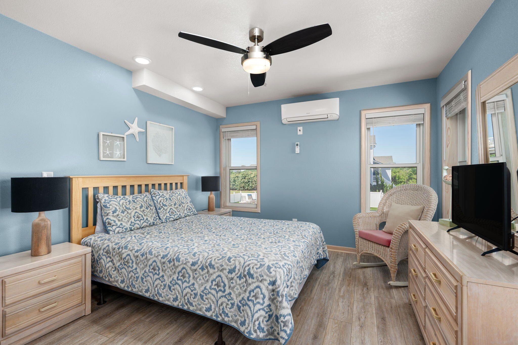 Une chambre à coucher comprenant un lit, des tables de chevet, une commode, un téléviseur, un ventilateur de plafond et une fenêtre donnant sur un paysage agréable.