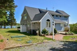 A two-story house with a sloped roof, a front porch, and a small garden area. - Waterfront with Private Dock! (Eastham)
