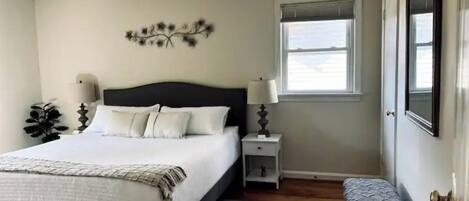 A bedroom with a bed, bedside tables, a bench, a window, and a wall decoration.