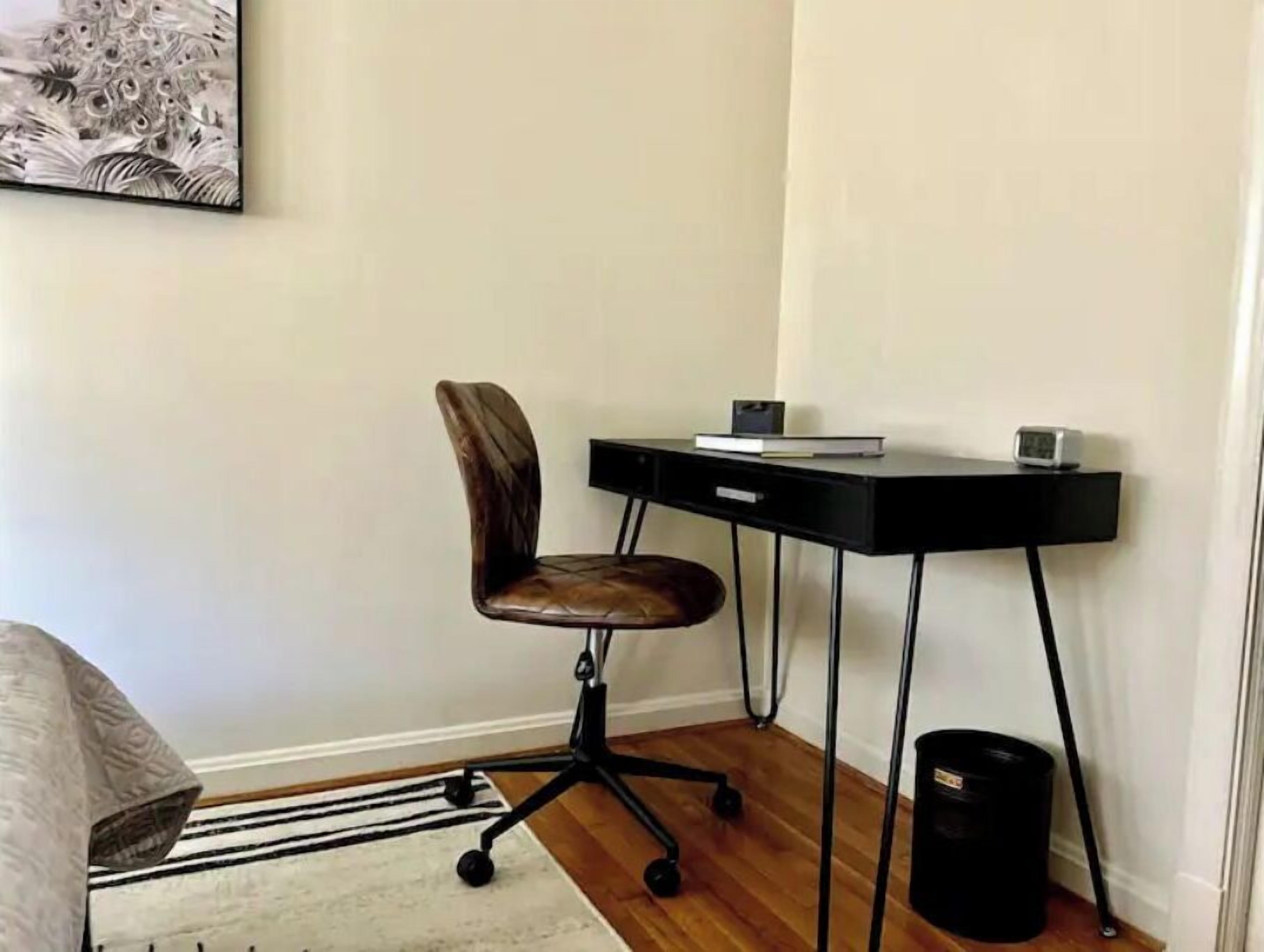 A corner room with a desk, chair, and a black trash bin.