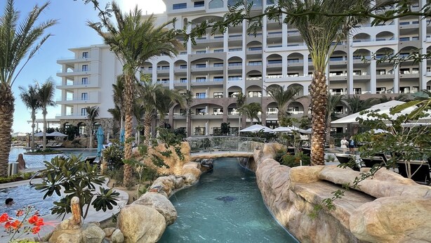 A resort with a pool area, palm trees, and a multi-story building in the background. - 9666llkhll (San Jose del Cabo)