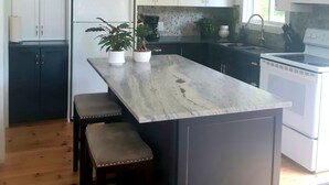 Una cocina con armarios blancos, una isla de mármol, un refrigerador, un fregadero y una estufa.