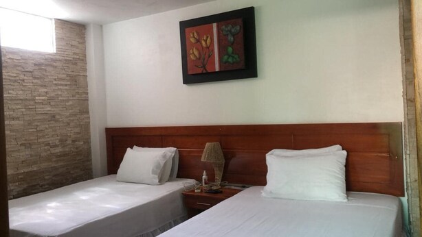 Habitación de hotel con dos camas, cabecero de madera, pared decorativa de piedra y una obra enmarcada sobre las camas.
