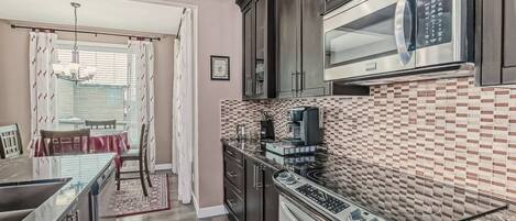 Una cocina moderna con armarios oscuros, un microondas, una estufa y un salpicadero de azulejos.