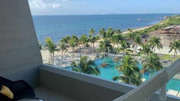A balcony with a hammock, a small table, and a view of the ocean and beach. - Luxurious Studio Playa Mujeres Cancun (Cancun)