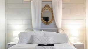 Een net opgemaakt bed met witte lakens en een zwart-wit gestreept deken, een gouden sierlijk spiegel erboven, en twee bedlampen op witte nachtkastjes.