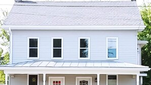 Une maison à deux étages avec un porche à l’avant, un garage et un petit jardin devant.