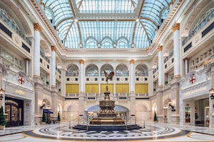 Un amplio vestíbulo de hotel con una fuente central, techos altos y una cúpula de cristal.
