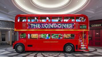 A red double-decker bus with "The Londoner" and "London Transport" on the side, parked indoors with a checkered floor and a circular ceiling design.